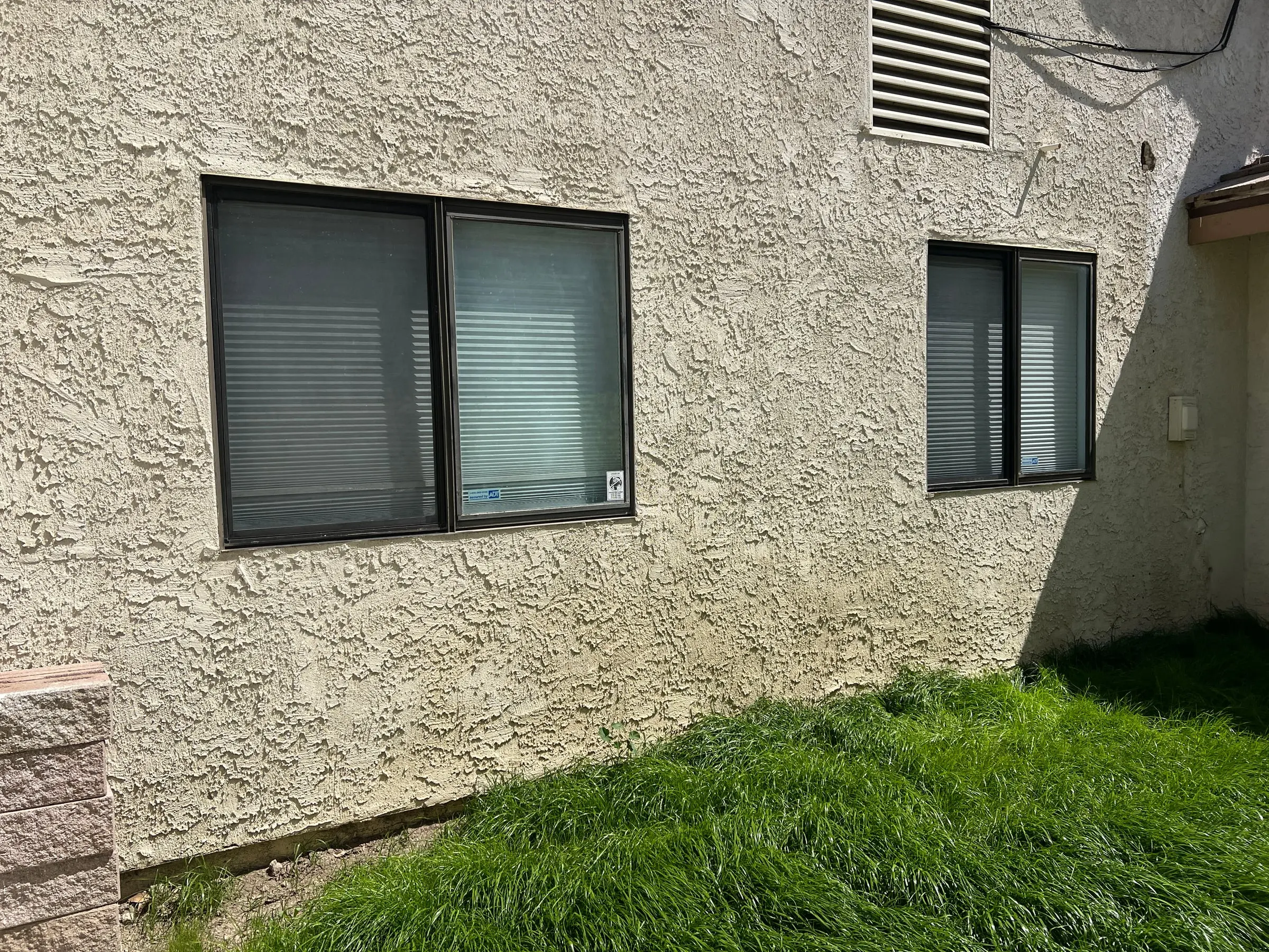 Two older windows in a stucco wall before replacement