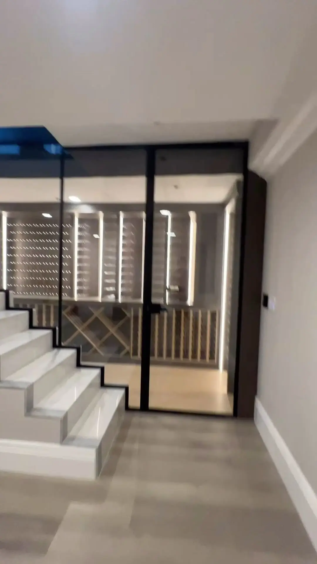 Wine room glass enclosure with black framed door beside a staircase